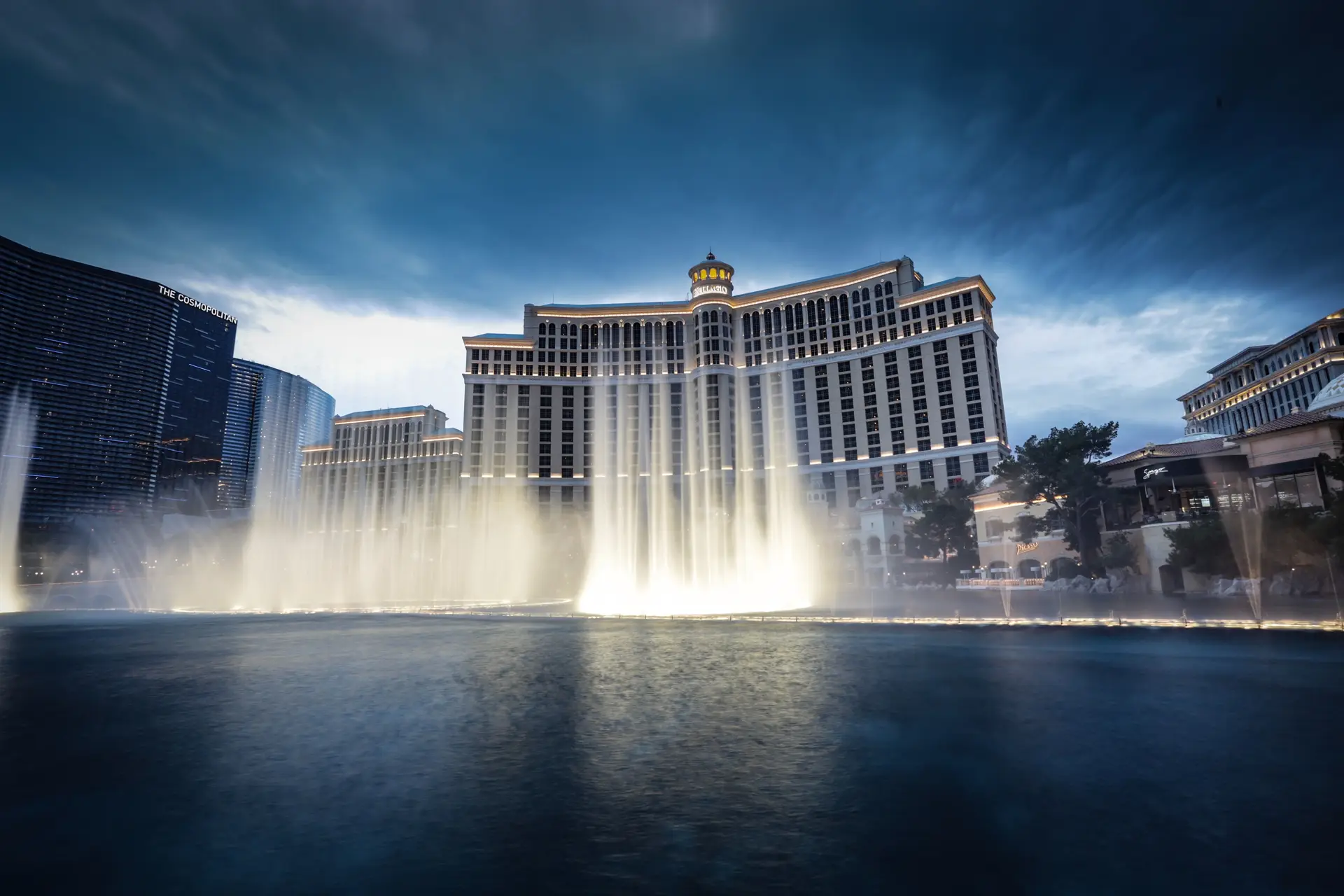 Illuminated resort fountain spectacle framed by luxury casino tower lights at dusk